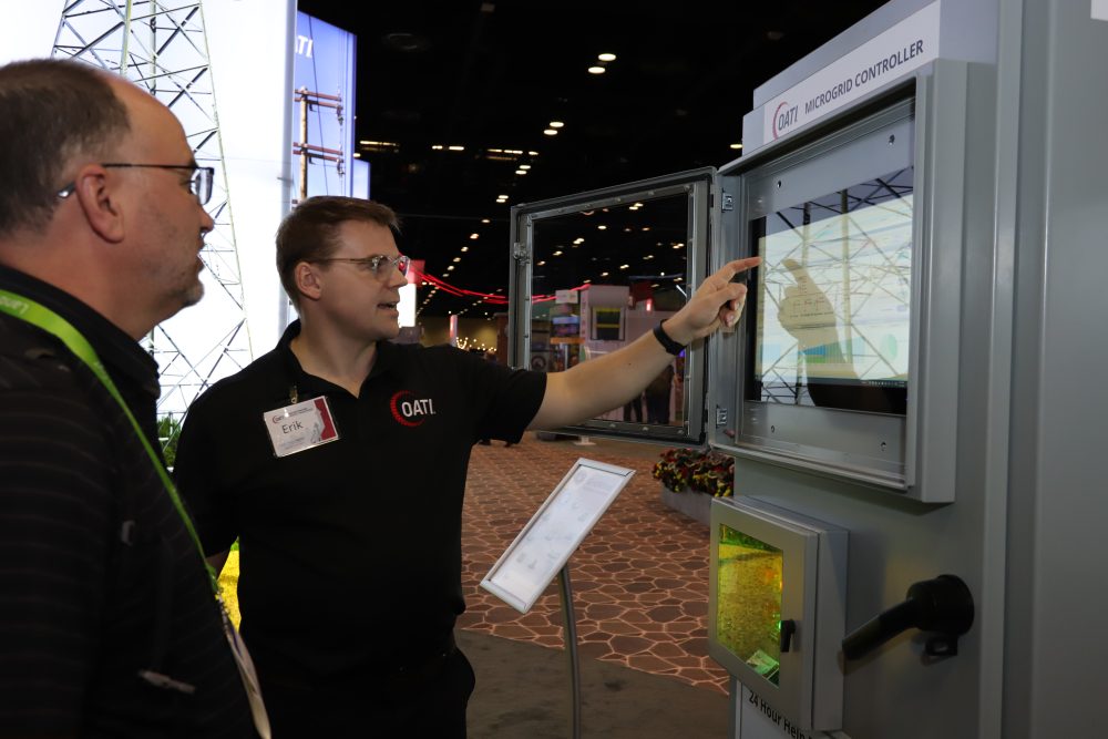 An OATI employee points at the OATI GridMind microgrid controller interface during a demo at a trade show.