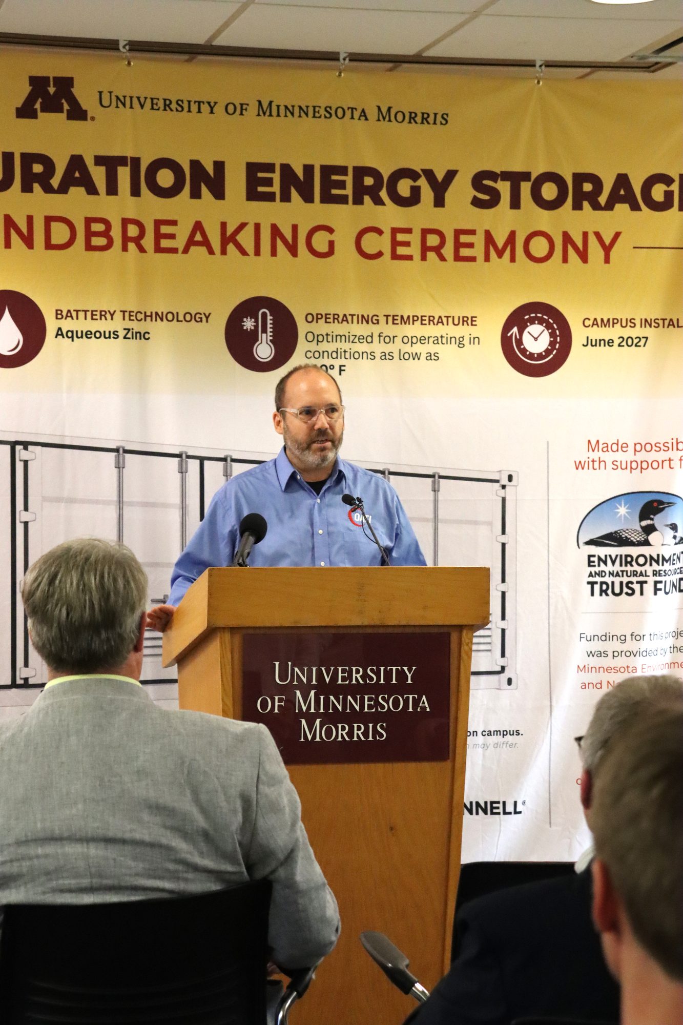 David Heim of OATI at the podium in front of the groundbreaking banner