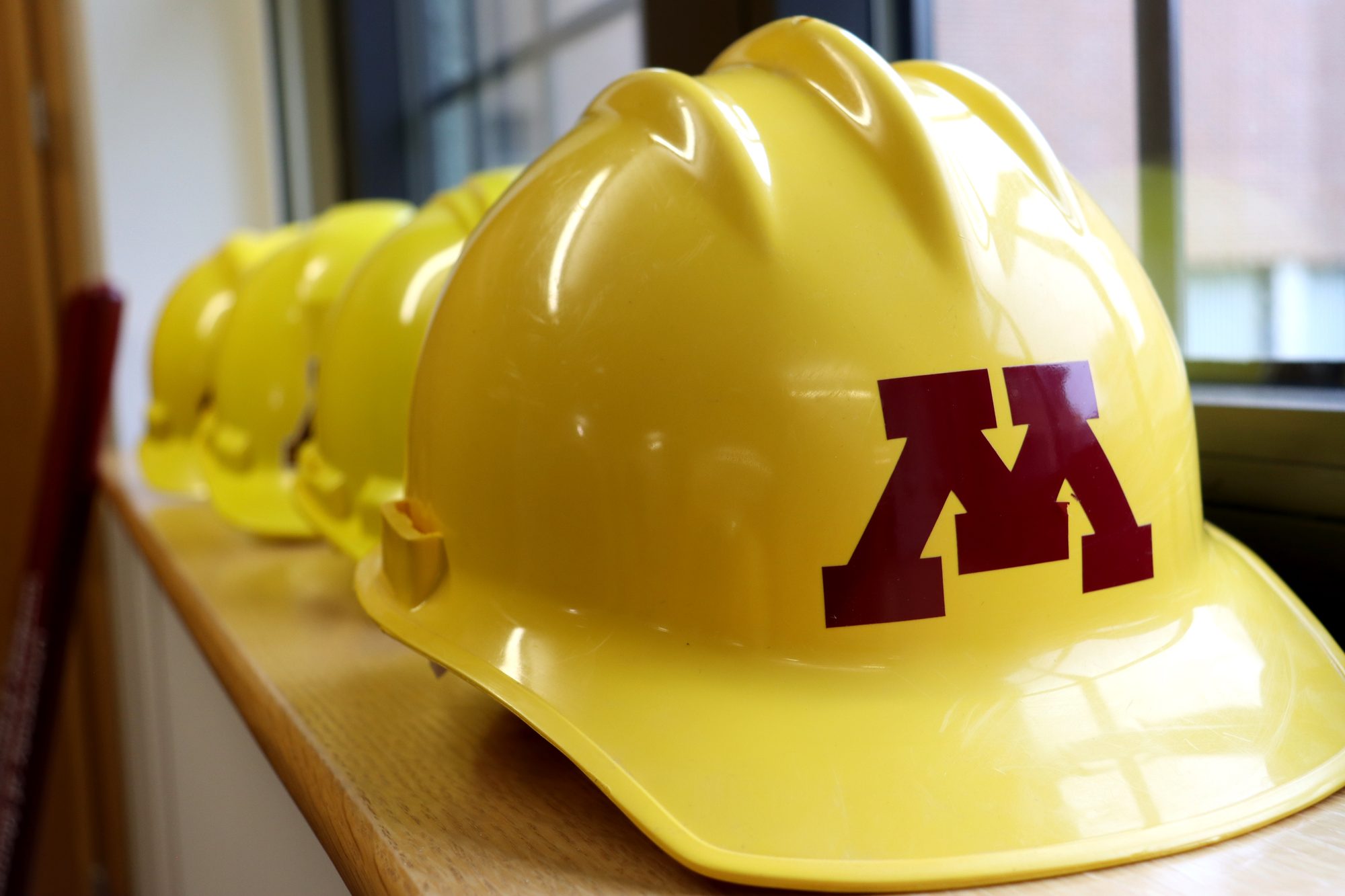 A row of yellow University of Minnesota hard hats on a windowsill