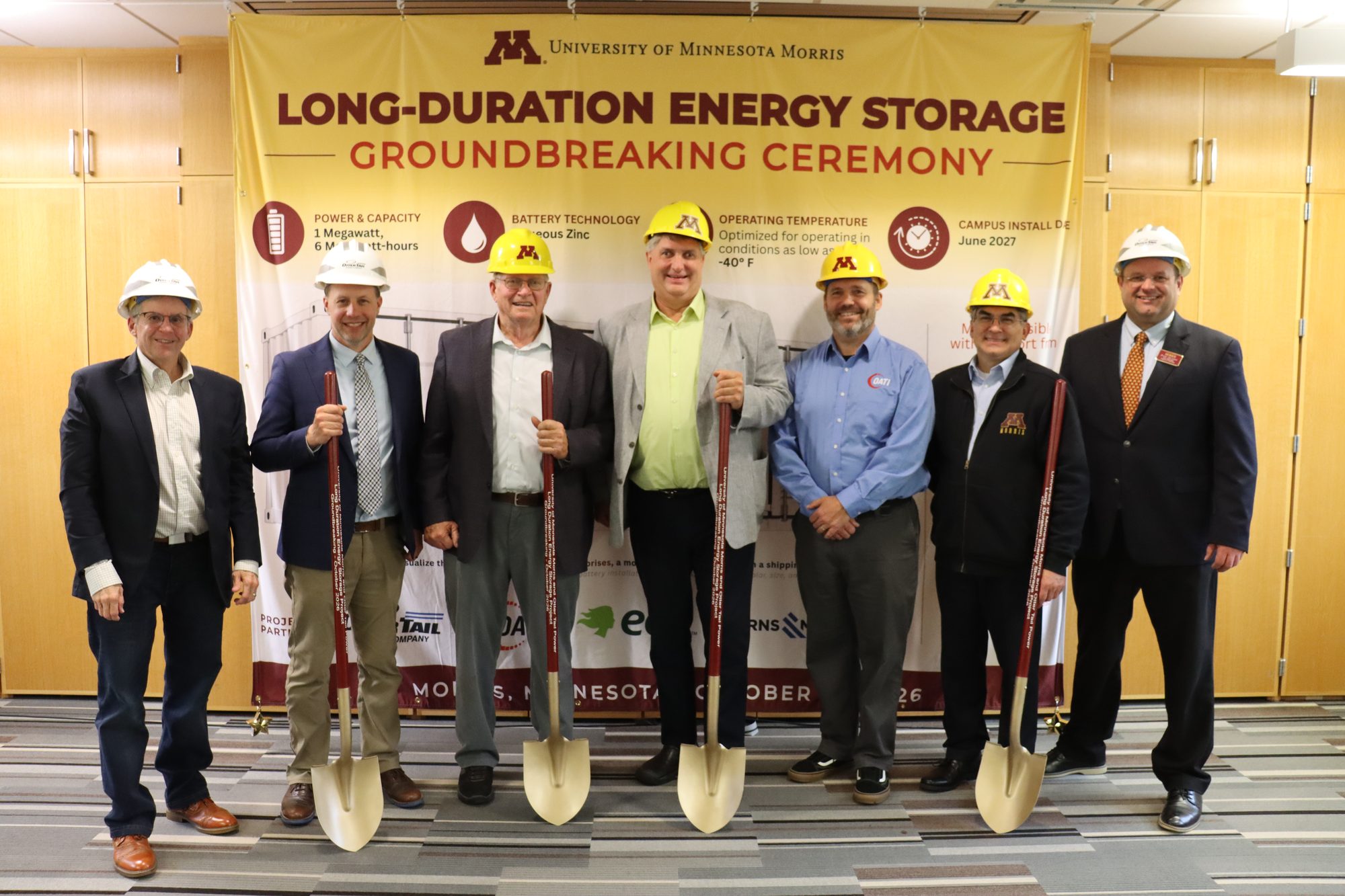 Project partners in hard hats with ceremonial shovels in front of the long-duration energy storage groundbreaking banner at the University of Minnesota Morris