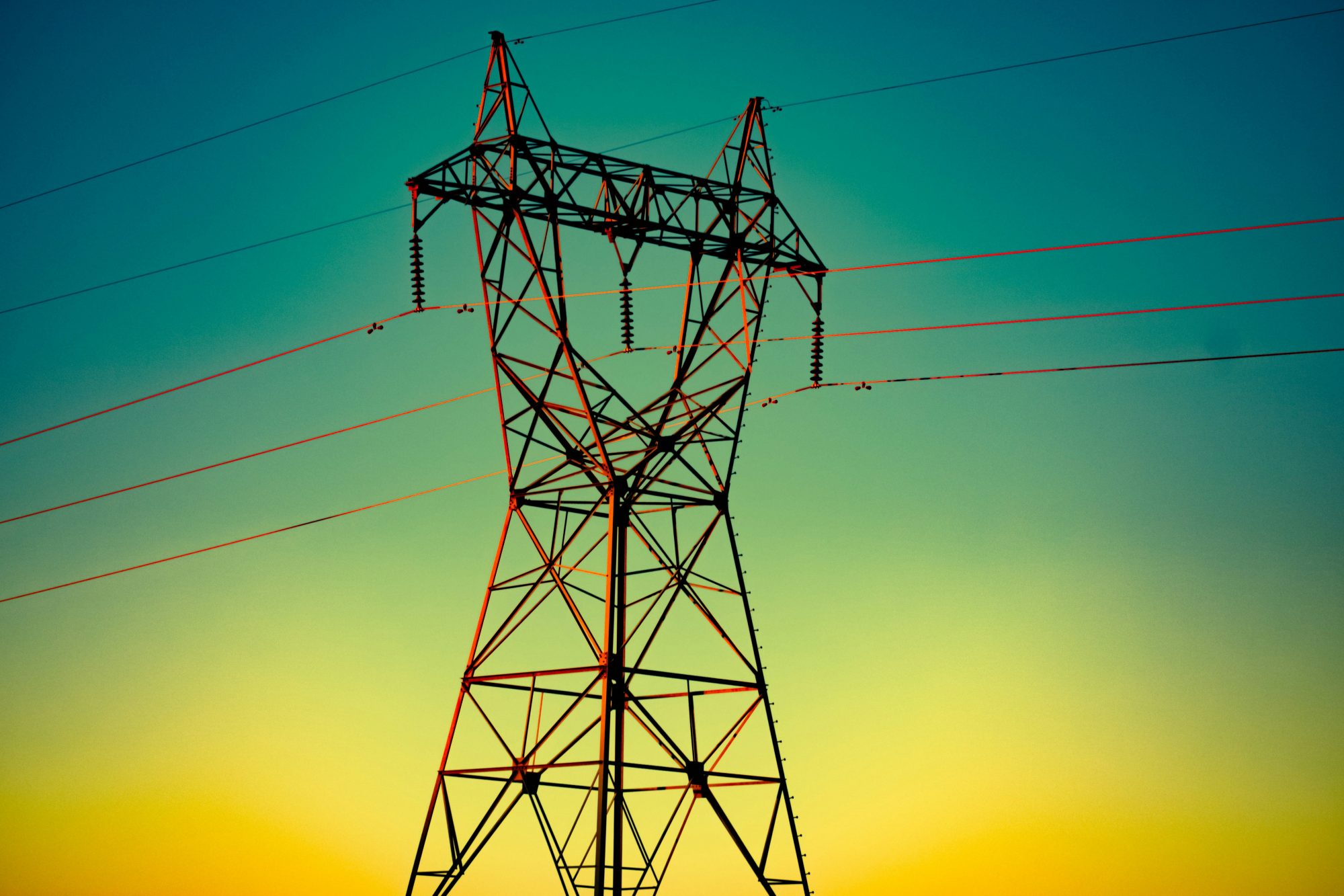Steel transmission tower and power lines against a green and yellow sky